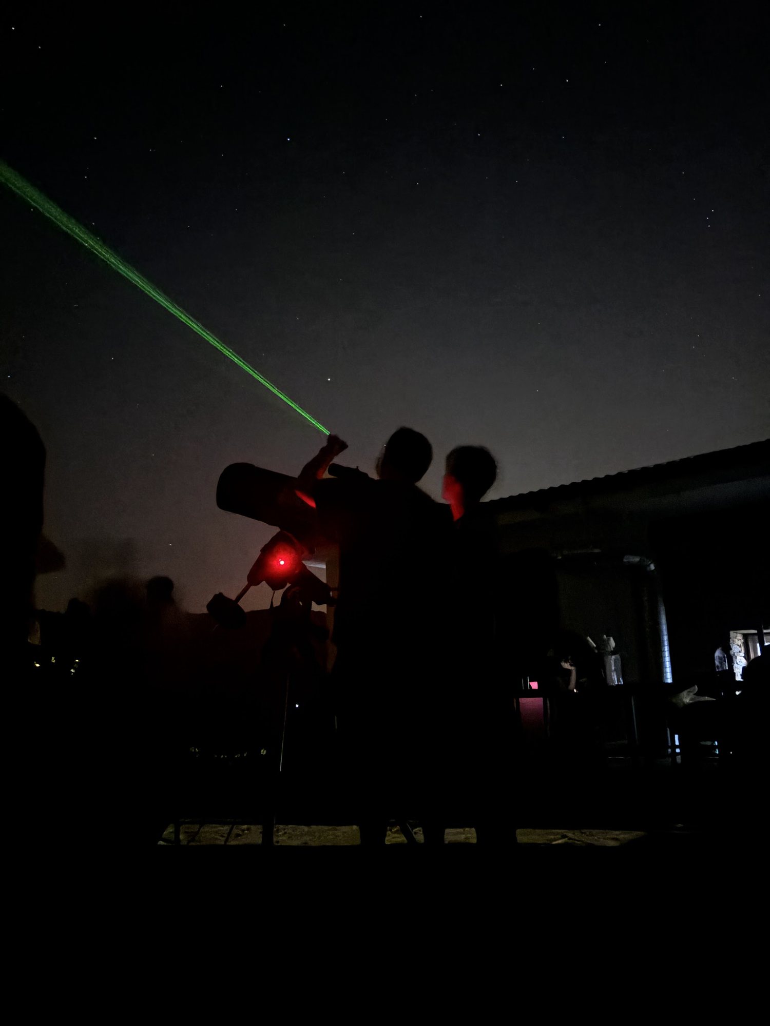 Gece gözleminde, teleskobun yanında yeşil lazerle gökyüzünü gösteren eğitmen